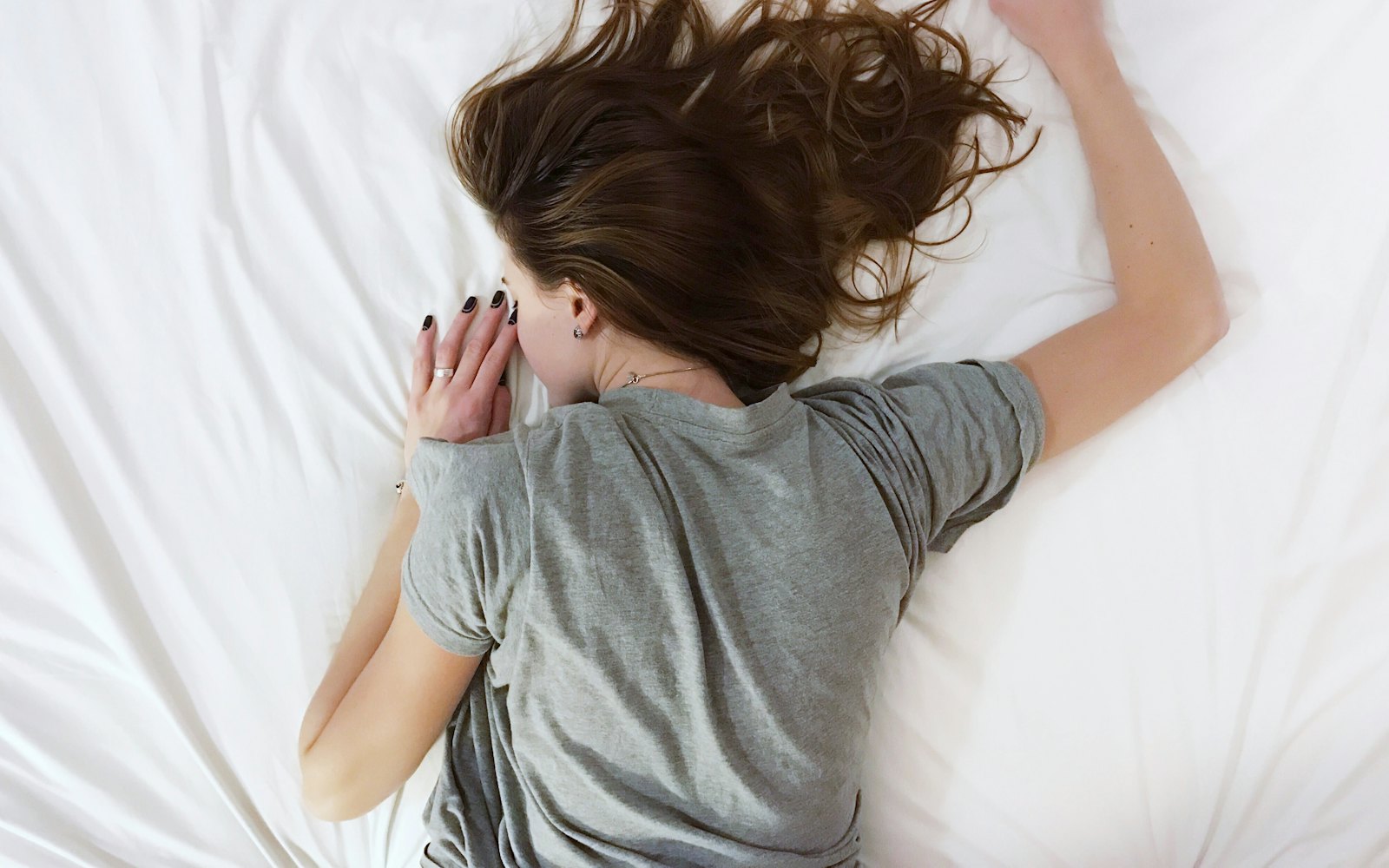 A woman lying face down on an unmade bed in a gray T-shirt
