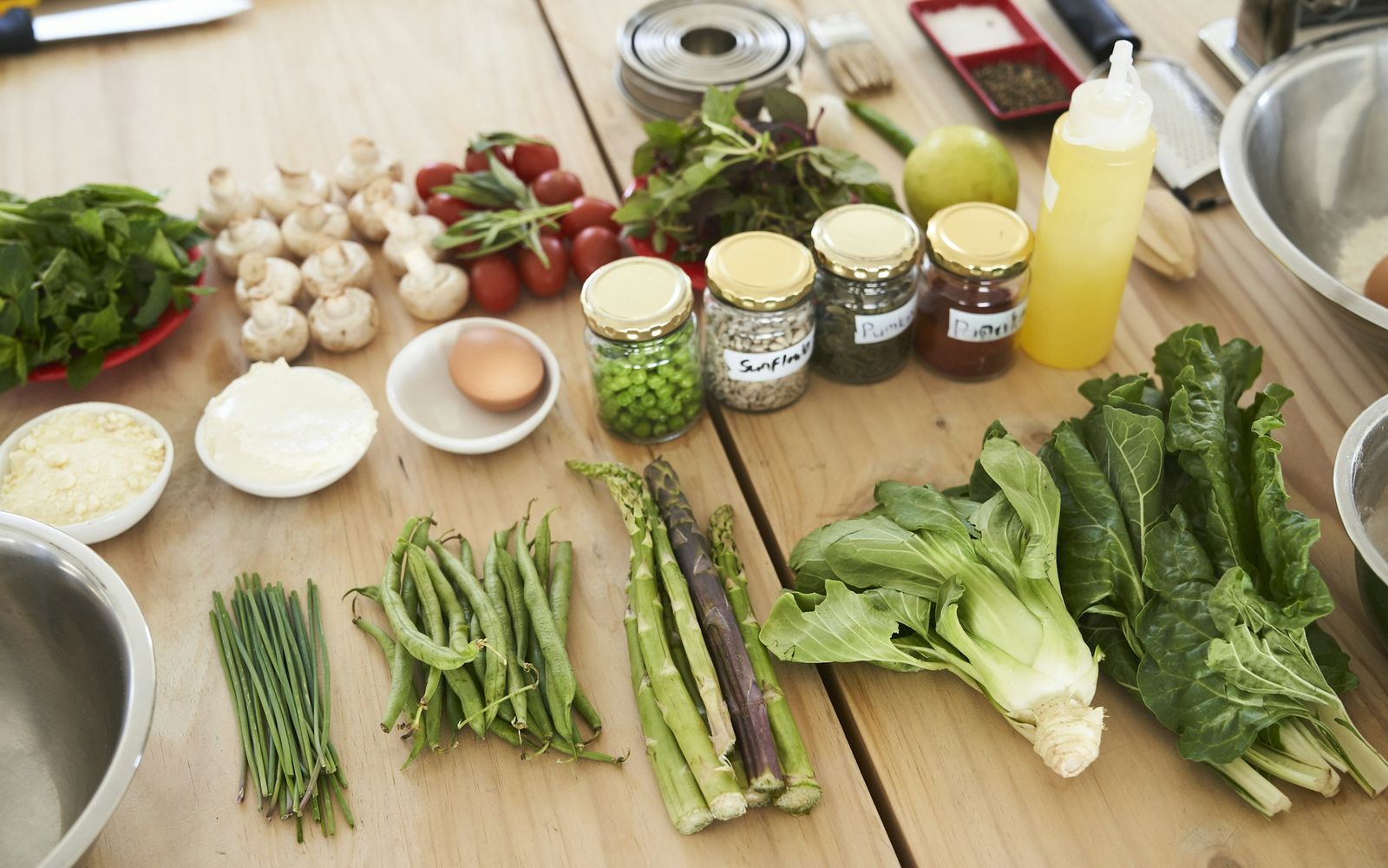 Fresh vegetables, eggs and jars of spices laid out on a wooden kitchen table