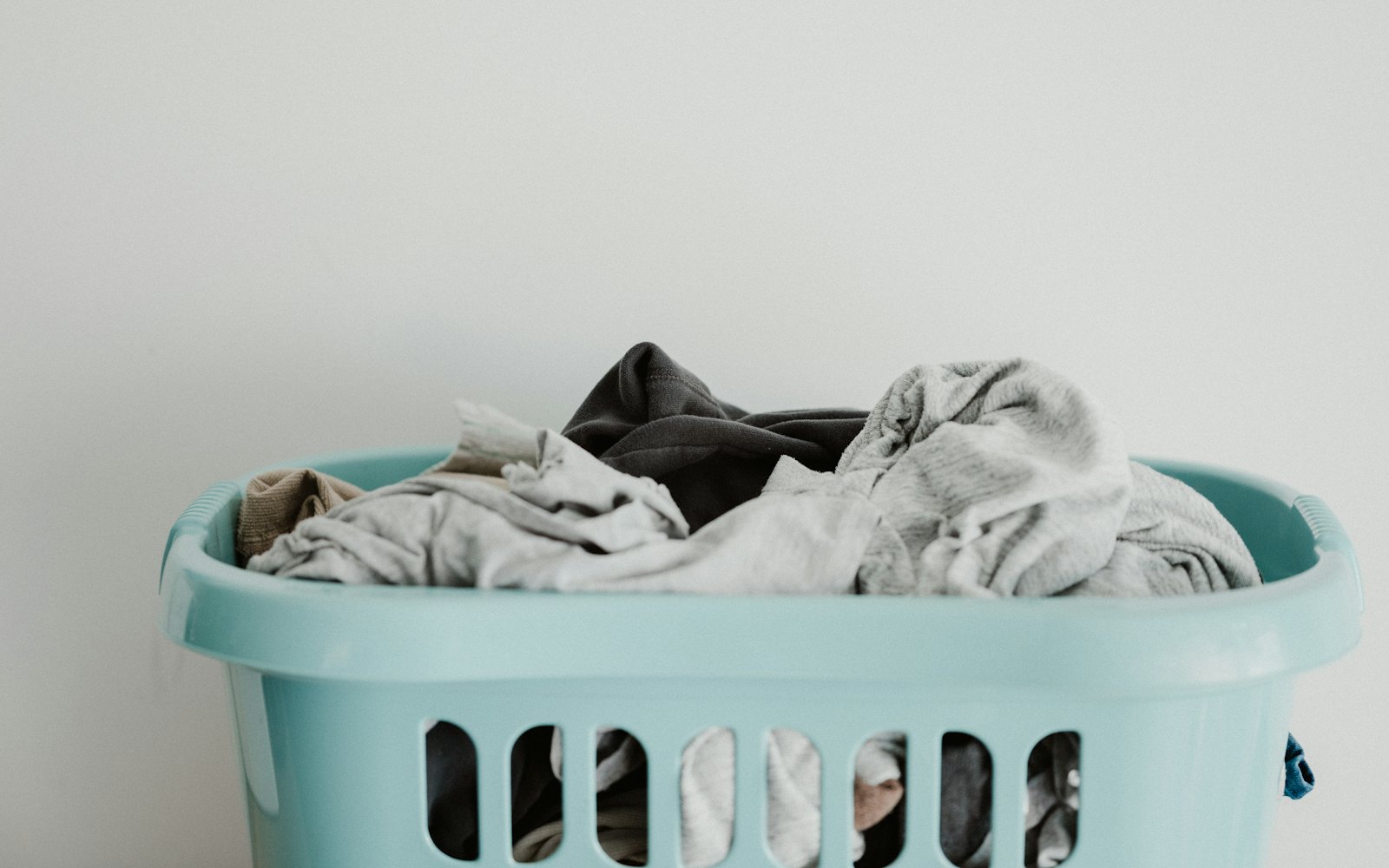 A light blue laundry basket full of clean clothes against a pale wall