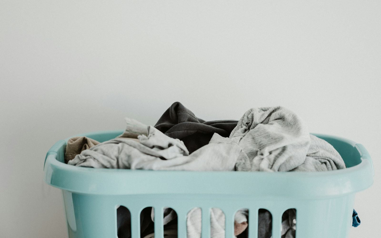 A light blue laundry basket full of clothes against a white wall