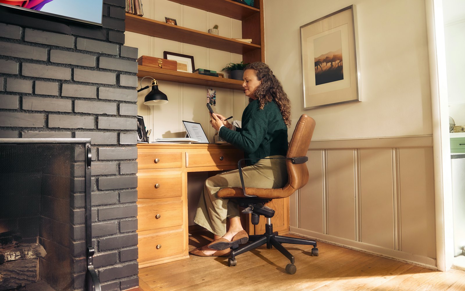 A woman working at a wooden desk in a warm, cozy home office