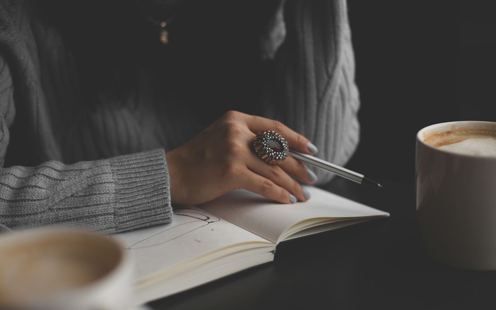 A hand holding a pen over an open notebook next to a cup of coffee