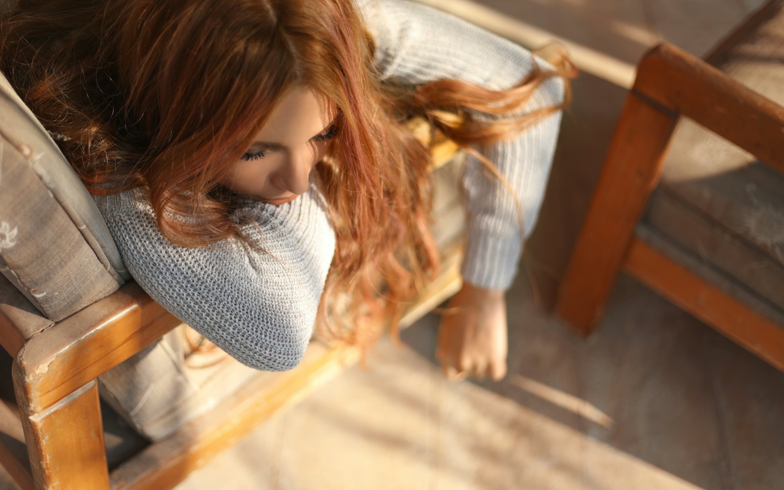 A woman asleep in a wooden armchair in warm afternoon light, her face turned away