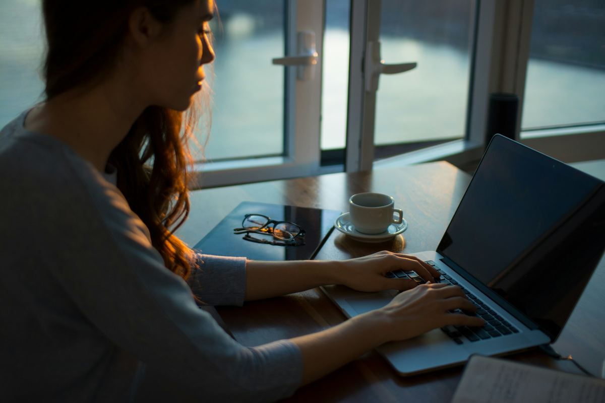 A woman working on a laptop by a window in the evening